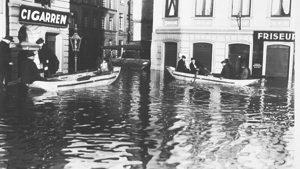 Zwei Boote auf dem überfluteten Holzmarkt beim Hochwasser 1920. Im Hintergrund sind ein Cigarrengeschäft und ein Friseurladen.