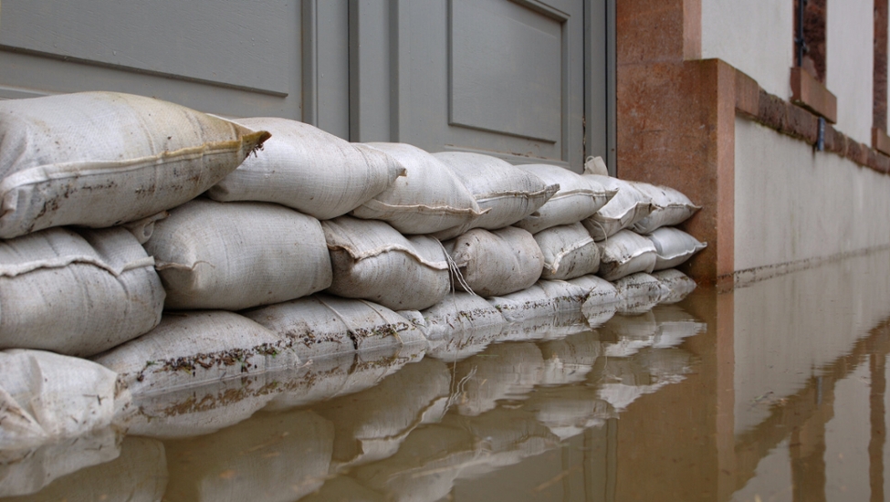 Tür, die mit Sandsäcken als Hochwasserschutz gesichert ist; im Vordergrund steht Wasser bis an die Sandsäcke.