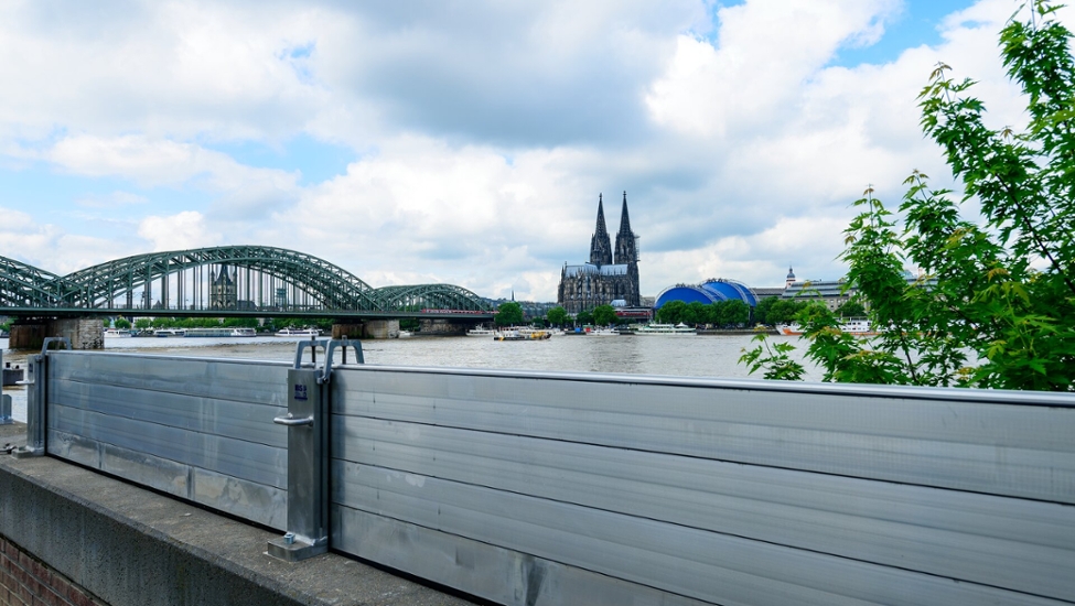 Kölner Dom, links daneben die Hohenzollernbrücke, aufgenommen von der rechten Rheinseite. Im Vordergrund steht eine Hochwasserschutzwand.
