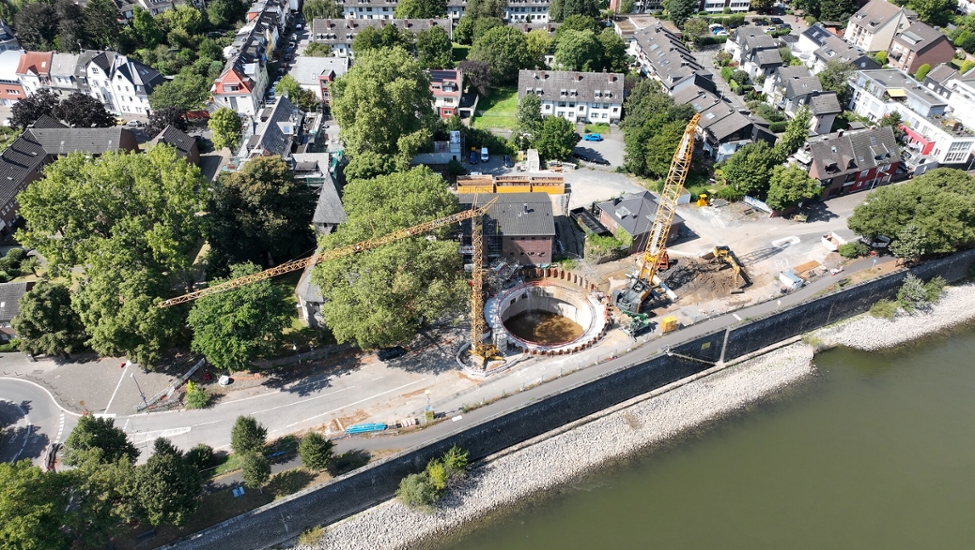Eine Luftbildaufnahme der Düker Baugrube in Niehl. Das Foto wurde von einer Drohne über dem Rhein aufgenommen. Neben der Baugrube stehen zwei Kräne.