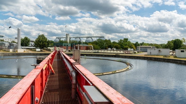 Rundräumer in einem Nachklärbecken, dahinter fünf Faulbehälter auf einem Klärwerksgelände.